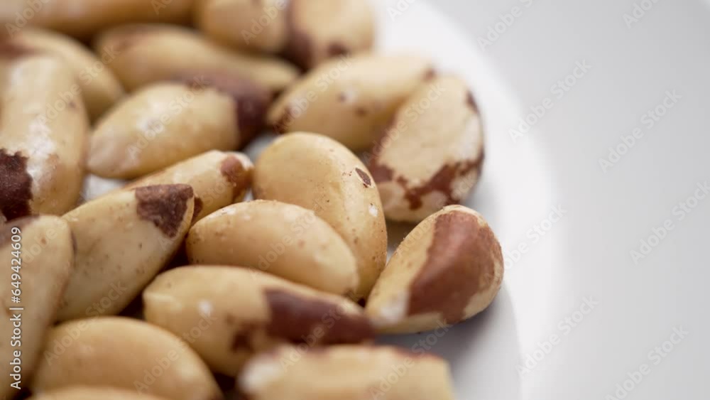 Brazil nuts heap on a white ceramic surface. Vegan, vegetarian nutritious food concept. Rotation Brazil nuts heap on a white ceramic surface. Vegan, vegetarian nutritious food concept. Rotation