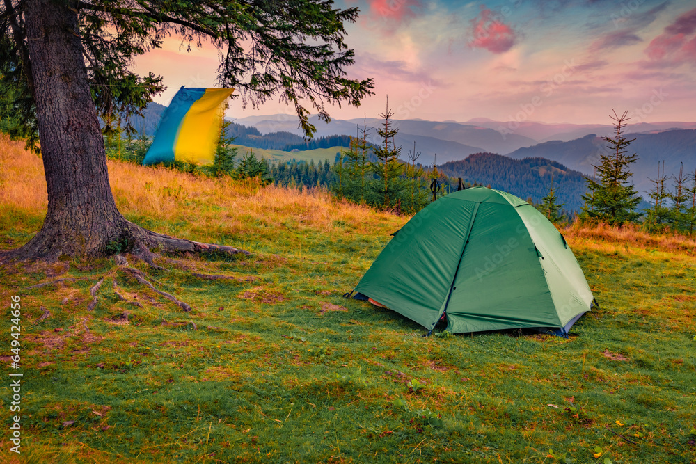 Green tent on the mountain meadow with Ukrainian flag waving on the wind. Fantastic sunrise in Carpathian mountains, Ukraine, Europe. Active tourism concept background..