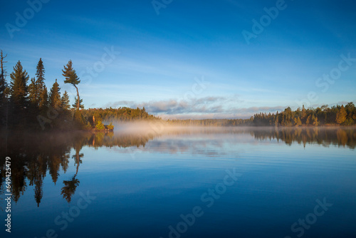 Beautiful blue lake with trees on a foggy morning in northern Minnesota at sunrise in September
