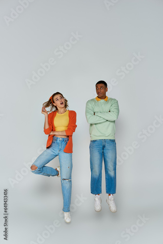 interracial couple in casual attire jumping and looking away on grey backdrop, action shot