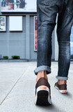 A male model walking through a pathway of a shopping mall wearing trendy jean and shoes...only showing his leg portion..