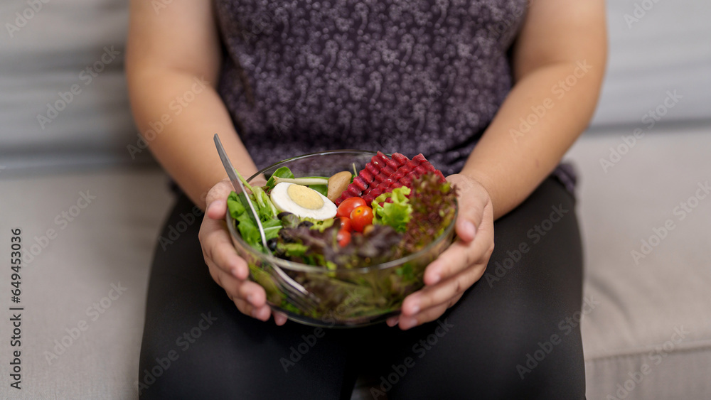 Overweight woman enjoy eating a bowl of vegetable salad at her home Overweight woman enjoy eating a bowl of vegetable salad at her home