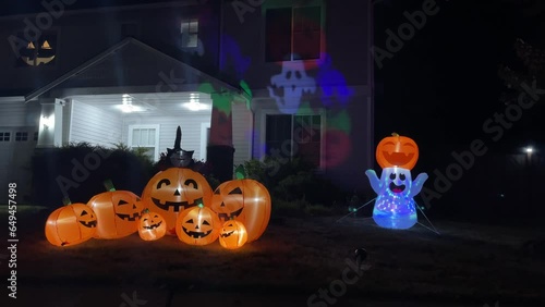 Illuminated night Halloween house outdoor decorations with inflatable figures of pumpkins, cat and ghost near house