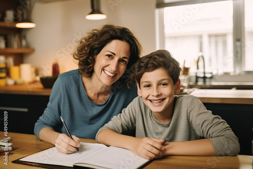 Cheerful mother doing homework with son at home photo