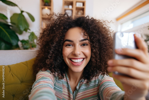 Happy Latin woman relaxing on the sofa at home - Smiling girl taking selfie picture with smartphone