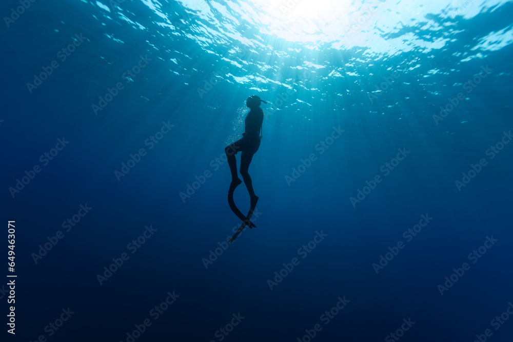 Freediver Swimming in Deep Sea With Sunrays. Young Man DIver Eploring Sea Life. Freediver Swimming in Deep Sea With Sunrays. Young Man DIver Eploring Sea Life.