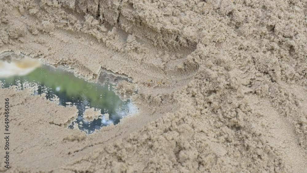 A woman's hand cleans wet sand from a mirror