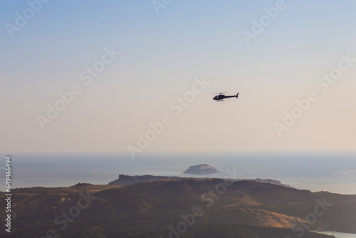 Helicopter flying over the volcanic Santorini island on a sunset sky