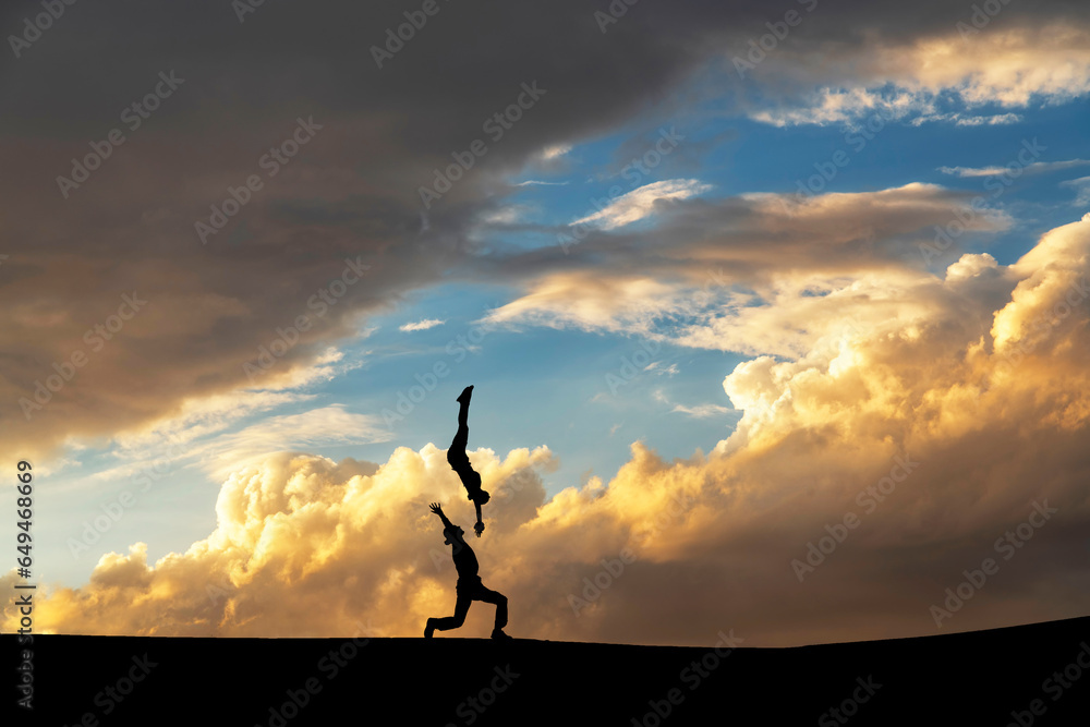 A couple dances on the top of a mountain against a bright sunset background.
