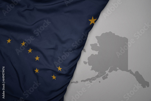 big waving national colorful flag and map of alaska state on the gray background. photo