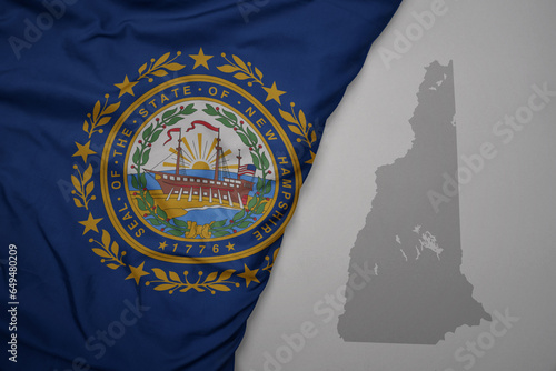 big waving national colorful flag and map of new hampshire state on the gray background. photo