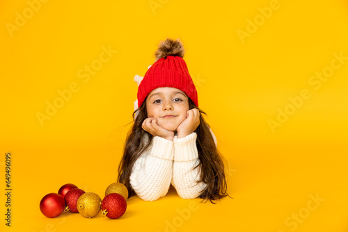 Funny child girl in a white sweatshirt and red knitted hat with pompom on a yellow background. The concept of children s emotions  joy and delight. Advertising clothing and sales. Ski resort vacation