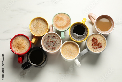 Many cups with different aromatic coffee on white marble table, flat lay