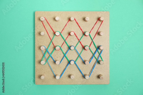 Wooden geoboard with rubber bands on green background, top view. Educational toy for motor skills development photo