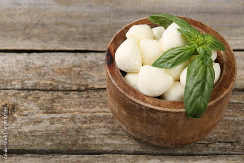 Tasty mozzarella balls and basil leaves in bowl on wooden table, closeup. Space for text