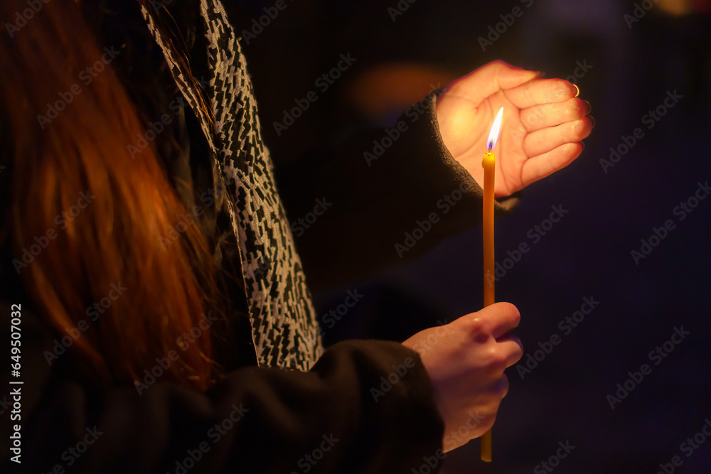 A candle in the hands of a praying woman. Symbolic concept. Background with selective focus - obrazy, fototapety, plakaty 