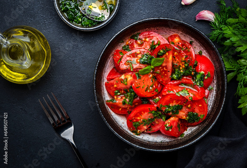 Summer vegan tomato salad with parsley, garlic, pepper and olive oil dressing, black table background, top view