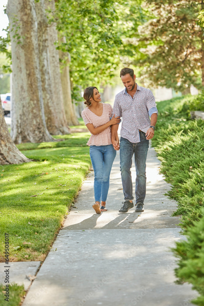 Smiling couple holding hands, walking on treelined sidewalk Smiling couple holding hands, walking on treelined sidewalk