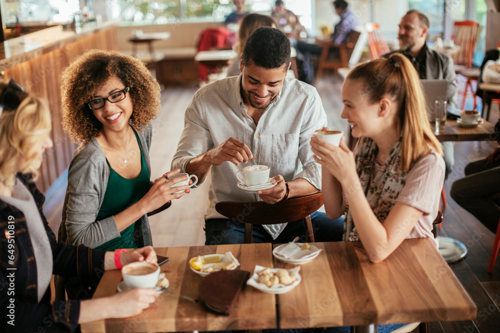 Young and diverse group of friends having a conversation over some coffee and desserts in a cafe