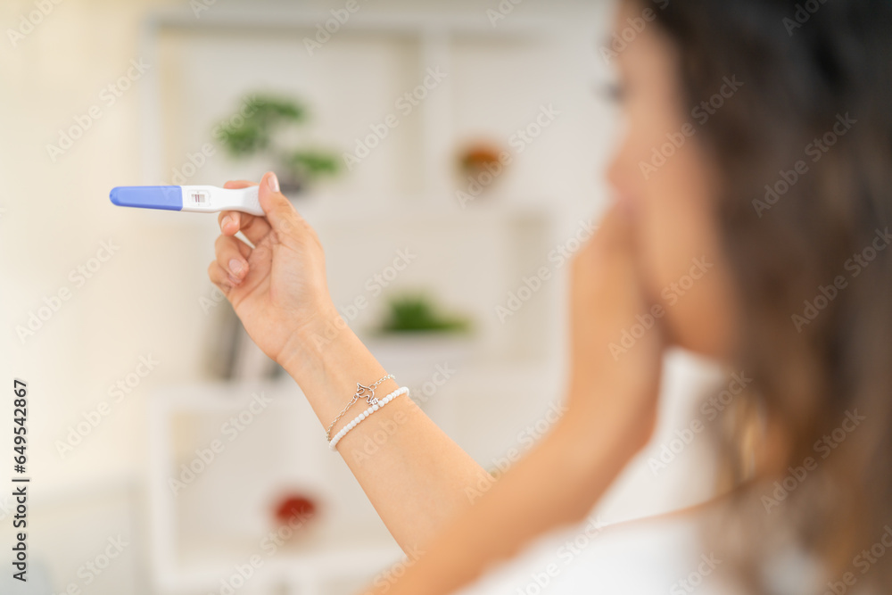 Rear view of surprised woman looking at a pregnancy test - obrazy, fototapety, plakaty 