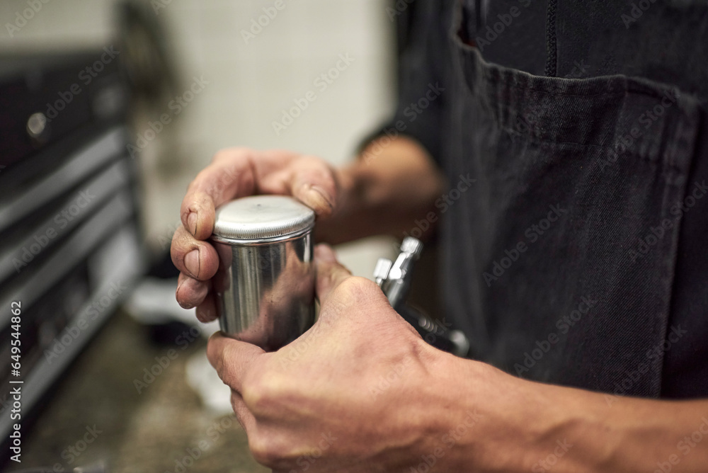 Hands of an unrecognizable young man closing the tank of a spray paint gun in his workshop. Close up view. Hands of an unrecognizable young man closing the tank of a spray paint gun in his workshop. Close up view.