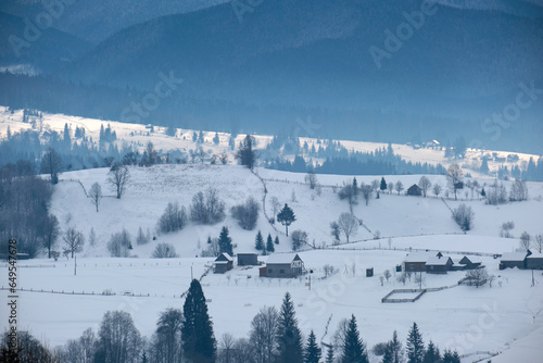 Winter landscape with small rural houses in remote settlement between snow covered forest in cold mountains