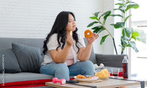 Asian young overweight oversized fat chubby plump unhealthy female teenager in casual outfit sitting thinking choosing between junk fastfood cola soft drink and dumbbell for exercise in living room