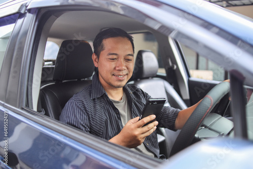 Smiling Asian man or driver driving car and using smartphone