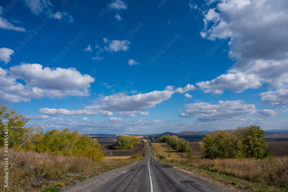 Road landscape. Empty track among mountains and fields in autumn. 