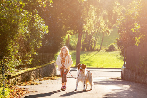 Little preschool girl walking with her dog. Cute kid and family pet in nature, fields and forest in late summer. Love and friendship between child and dog. Having fun together.