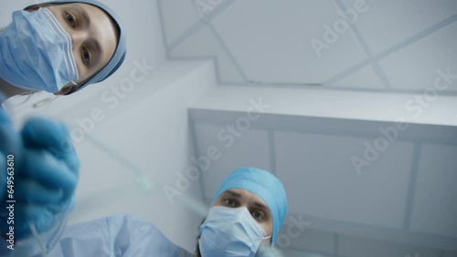 African American medic talk with patient about ondition. Adult doctor with female colleague puts breathing tube and drip. Professional surgeons take man on gurney to surgery down hospital corridor.