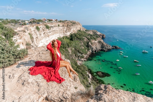 Woman red dress sea. Happy woman in a red dress and white bikini sitting on a rocky outcrop, gazing out at the sea with boats and yachts in the background.