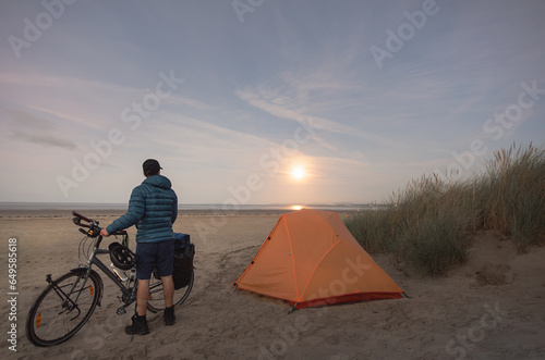 man with touring bike camping on beach under full moon