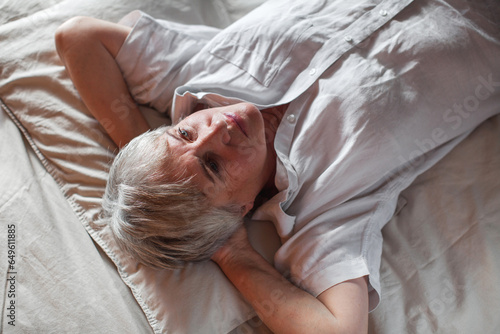 Sad unhappy senior woman seated on bed in bedroom photo