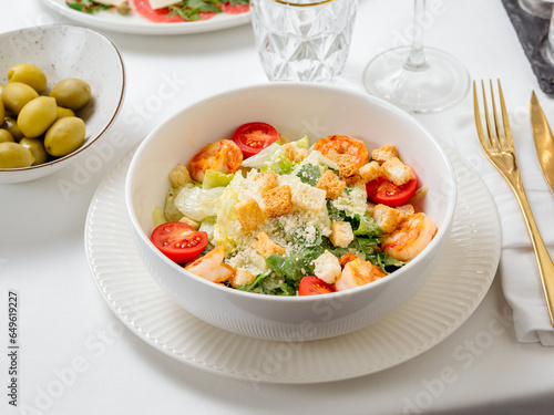 Caesar salad with shrimps on plate in restaurant table interior. Classic caesar shrimp salad closeup view