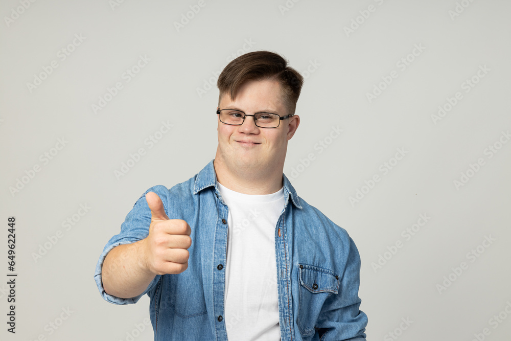 A smiling young man with cerebral palsy in glasses, jeans and a white T-shirt poses for the camera. World Genetic Diseases Day concept A smiling young man with cerebral palsy in glasses, jeans and a white T-shirt poses for the camera. World Genetic Diseases Day concept