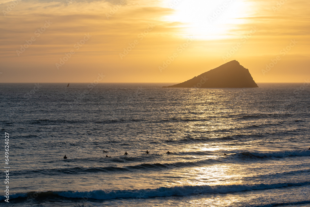Sunset over the Great Mewstone with surfers in the foreground at Wembury beach in Devon, UK. Sunset over the Great Mewstone with surfers in the foreground at Wembury beach in Devon, UK.
