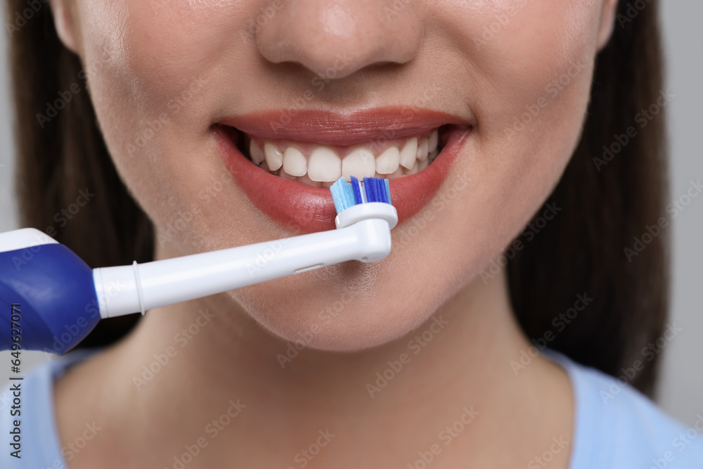 Woman brushing her teeth with electric toothbrush on light grey background, closeup Woman brushing her teeth with electric toothbrush on light grey background, closeup