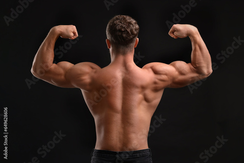 Muscular man showing his strength on black background, back view. Sexy body