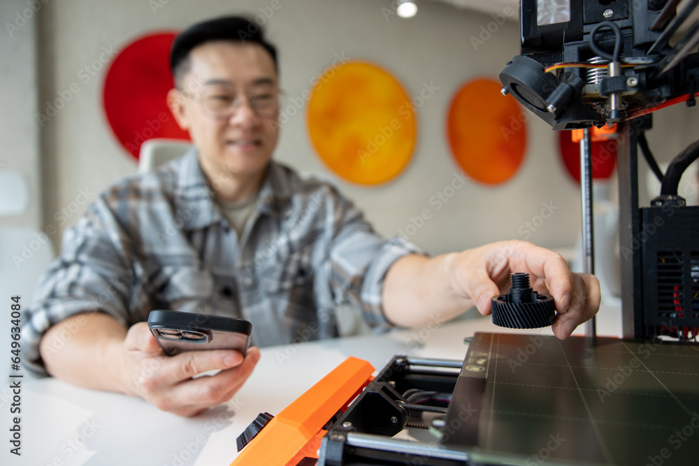 Man designer holding deteil printed on 3D printer working in engineering workshop.