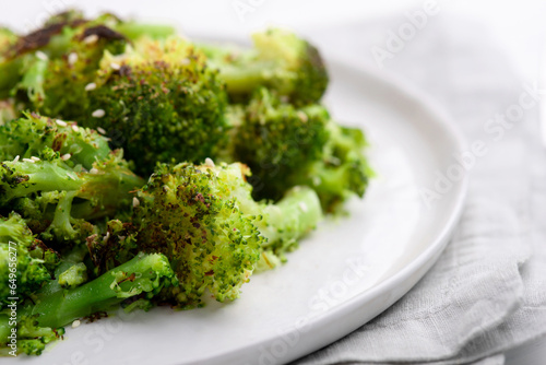 Broccoli inflorescences fried with spices and sesame seeds on a plate on a white table. Close up.
