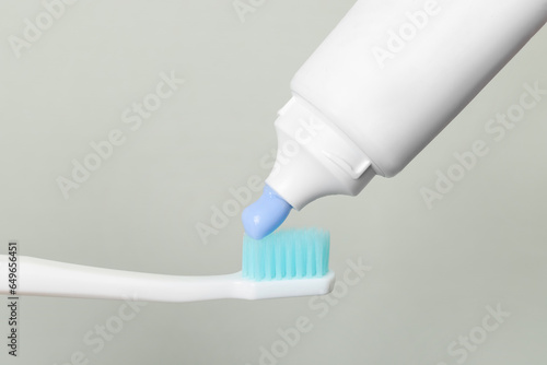 Applying paste on toothbrush against grey background