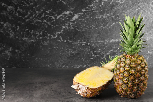 Whole and cut ripe pineapples on grey table near black wall, space for text