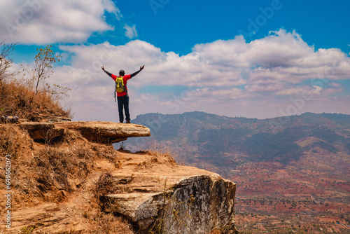 A hiker with arms outstretched standing on a rock at a scenic lookout against a valley in Mbooni Forest, Makueni County, Kenya photo