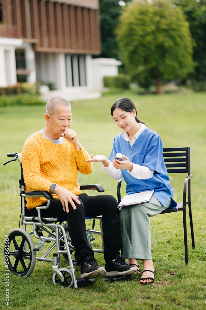 Elderly asian senior man on wheelchair with Asian careful caregiver and encourage patient, walking in garden. with care from a caregiver and senior health insurance.. Elderly asian senior man on wheelchair with Asian careful caregiver and encourage patient, walking in garden. with care from a caregiver and senior health insurance..