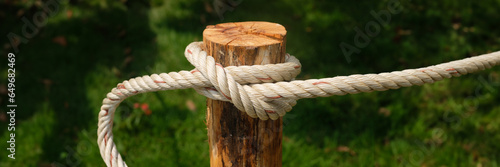 Close up white rope twisted on wooden pole with green bokeh background	