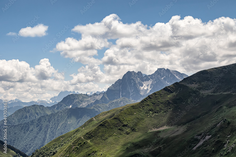 Fototapeta premium Mountain landscape with green slopes, cliffs, glaciers and white clouds in the sky