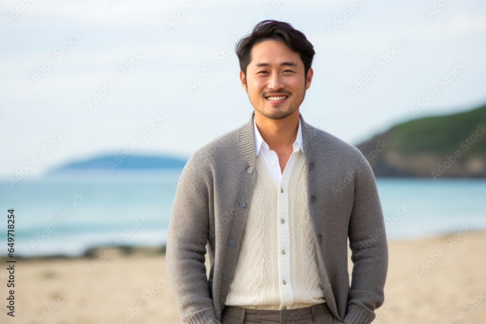 portrait of a confident Japanese man in his 30s wearing a chic cardigan against a beach background portrait of a confident Japanese man in his 30s wearing a chic cardigan against a beach background