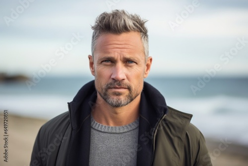 portrait of a serious, Polish man in his 40s wearing a chic cardigan against a beach background