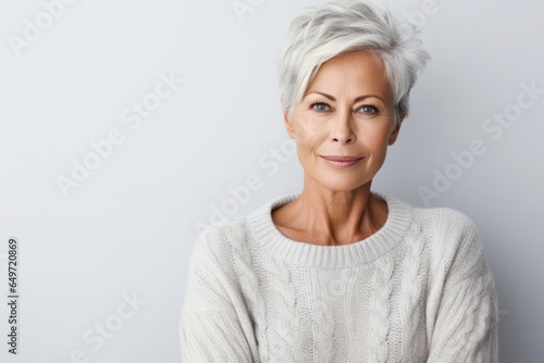 portrait of a serious, Polish woman in her 60s wearing a cozy sweater against a white background